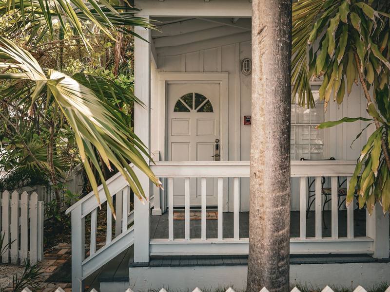 Front porch with a white door and white railing, framed by palm fronds