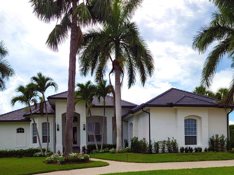 White single-story house with a dark tile roof, a green lawn, and palm trees under a blue sky