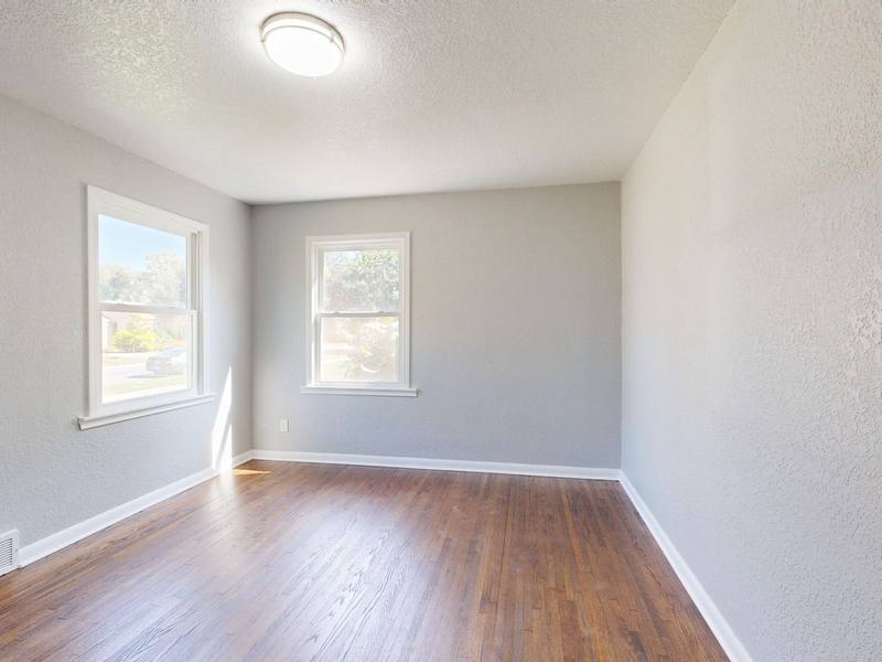 Empty bright room with hardwood floor, gray walls, and two windows
